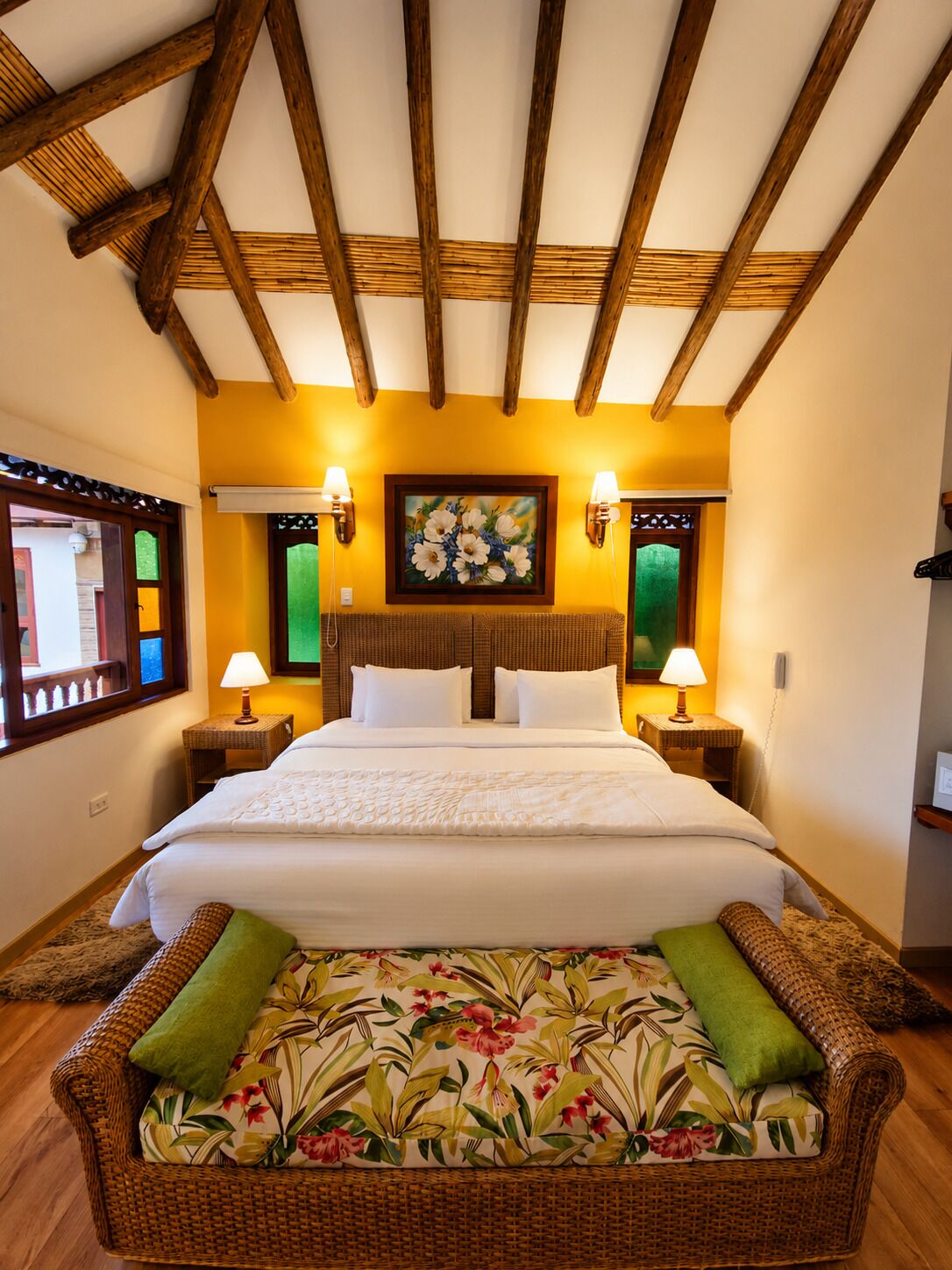 A hotel room with a bed, two nightstands, a painting, and a wicker sofa.