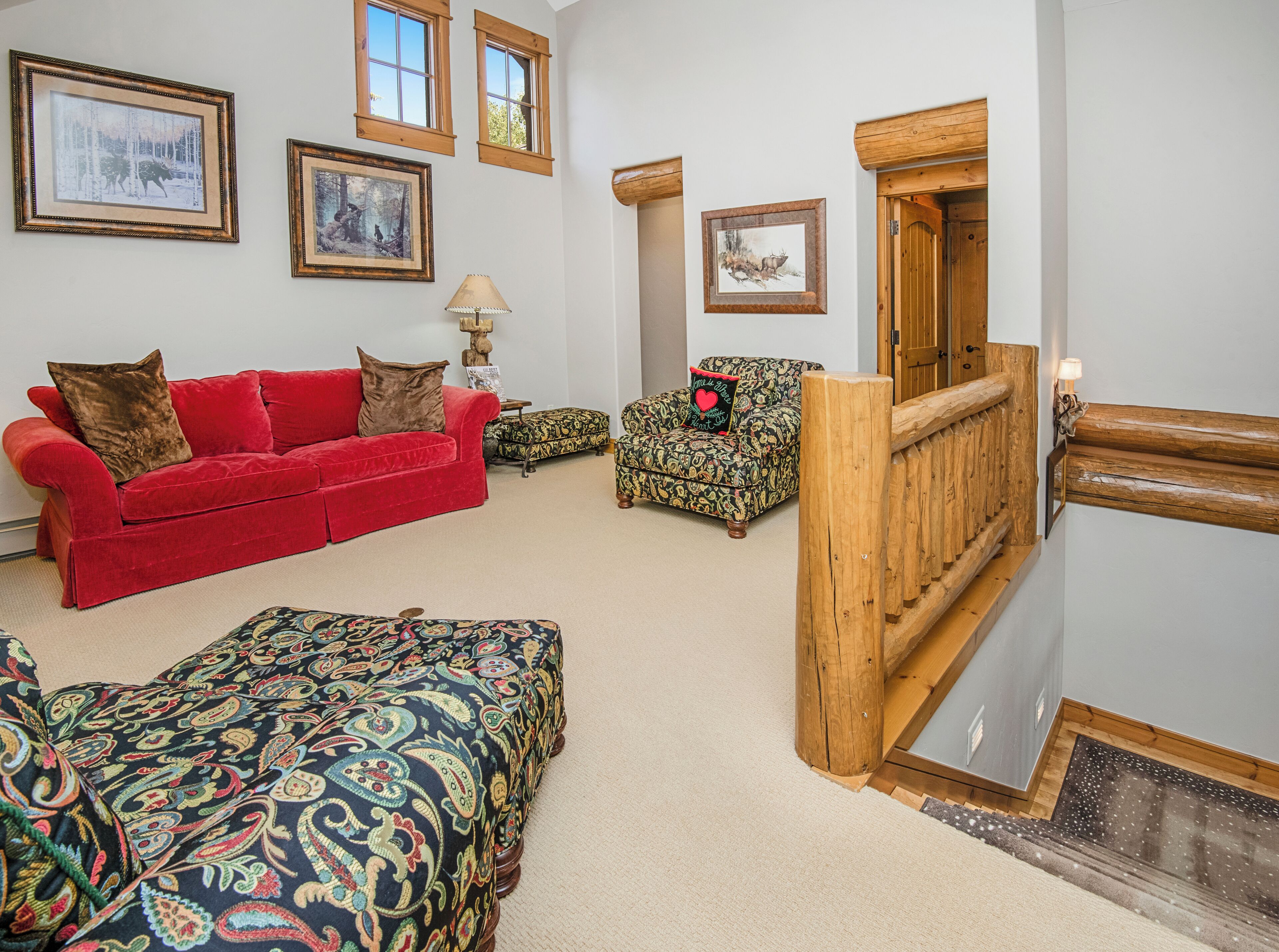 A cozy living room with a red sofa, patterned ottoman, and a wooden staircase.