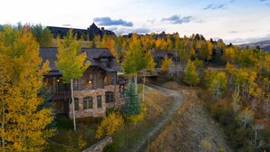 Un chalet doté d’une façade en pierre, de nombreuses fenêtres et d’un balcon donnant sur une zone boisée.