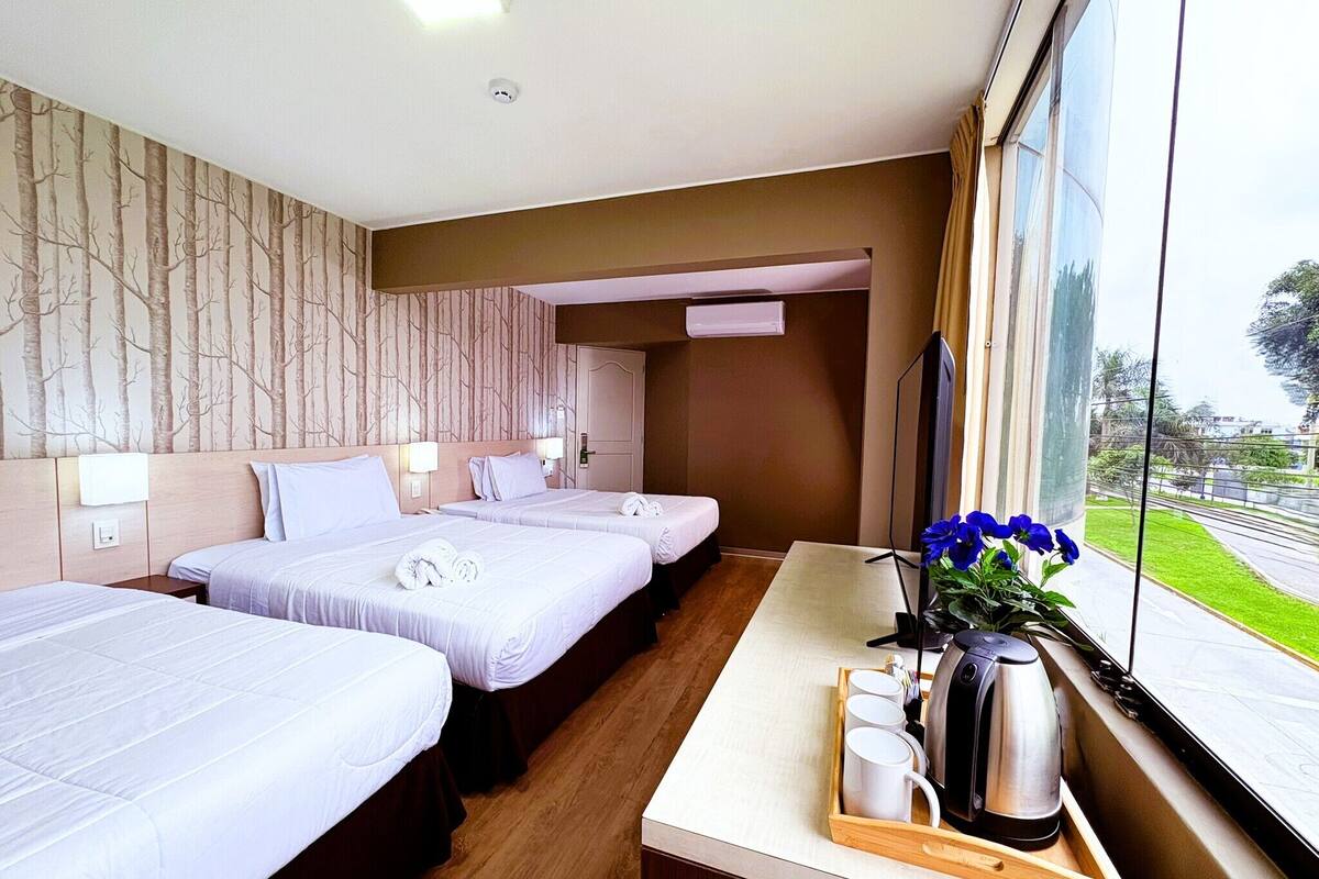 A hotel room with two beds, a wooden floor, a window with a view, a coffee station, and a wall with a tree pattern.