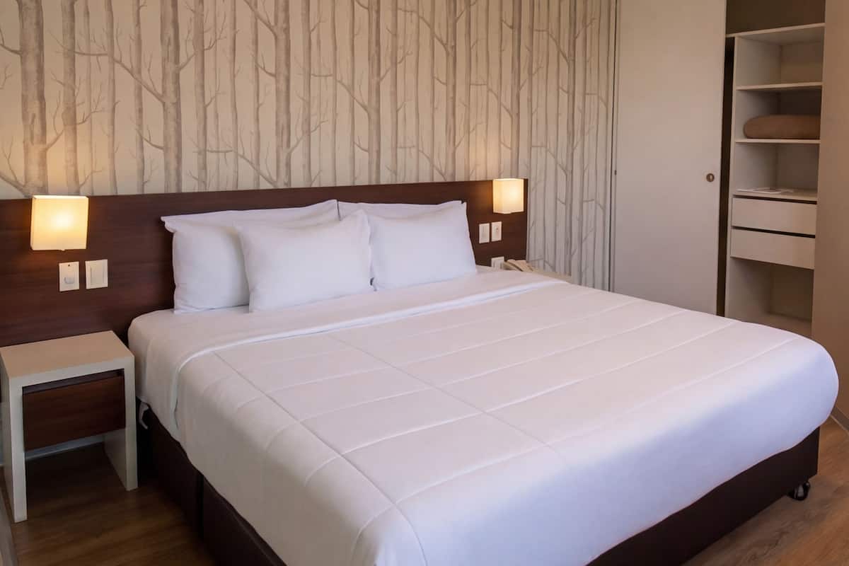 A hotel room with a large bed, two bedside tables, a wardrobe, and a wall with a tree pattern.