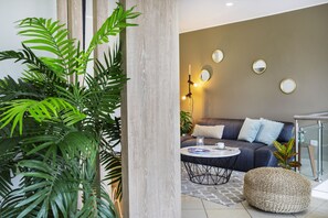 A modern living room with a sofa, round coffee table, and a large plant. - Palmetto Hotel Business La Perla (Callao)