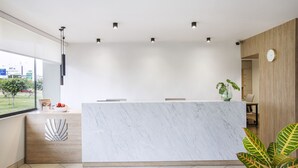A modern reception desk with a marble top, a wooden accent wall, and a large window offering a view of the outdoors. - Palmetto Hotel Business La Perla (Callao)
