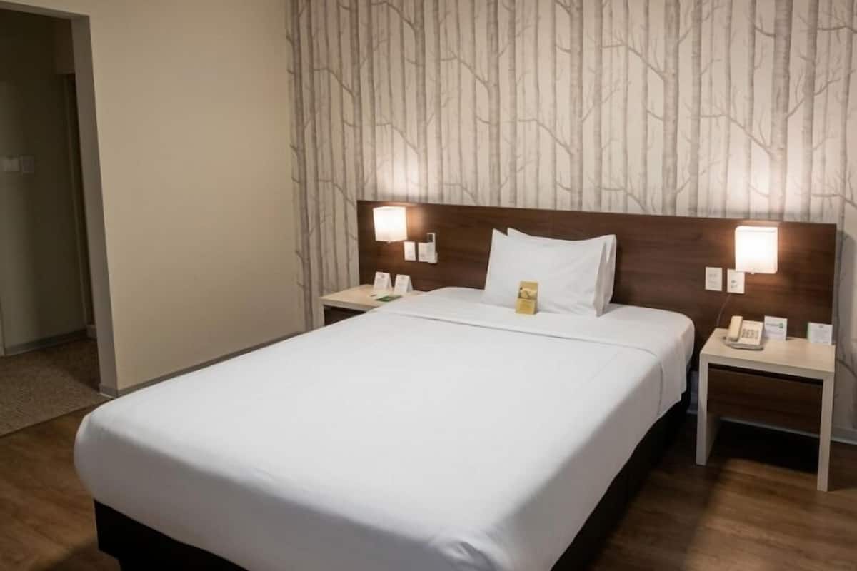 A hotel room with a large bed, two bedside tables, a headboard with a tree pattern, and a ceiling light.