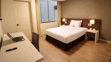 Habitación de hotel con cama, mesitas de noche, escritorio con computadora portátil, silla y ventana con cortinas.