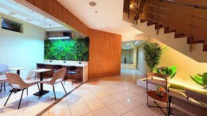 A modern lobby with a reception desk, seating area, staircase, and a green wall feature. - Palmetto Hotel Business La Perla (Callao)