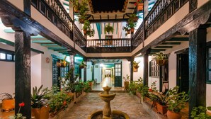 A courtyard with a central fountain, potted plants, and a balcony with hanging plants. - Hotel Antonio Nariño (Villa de Leyva)