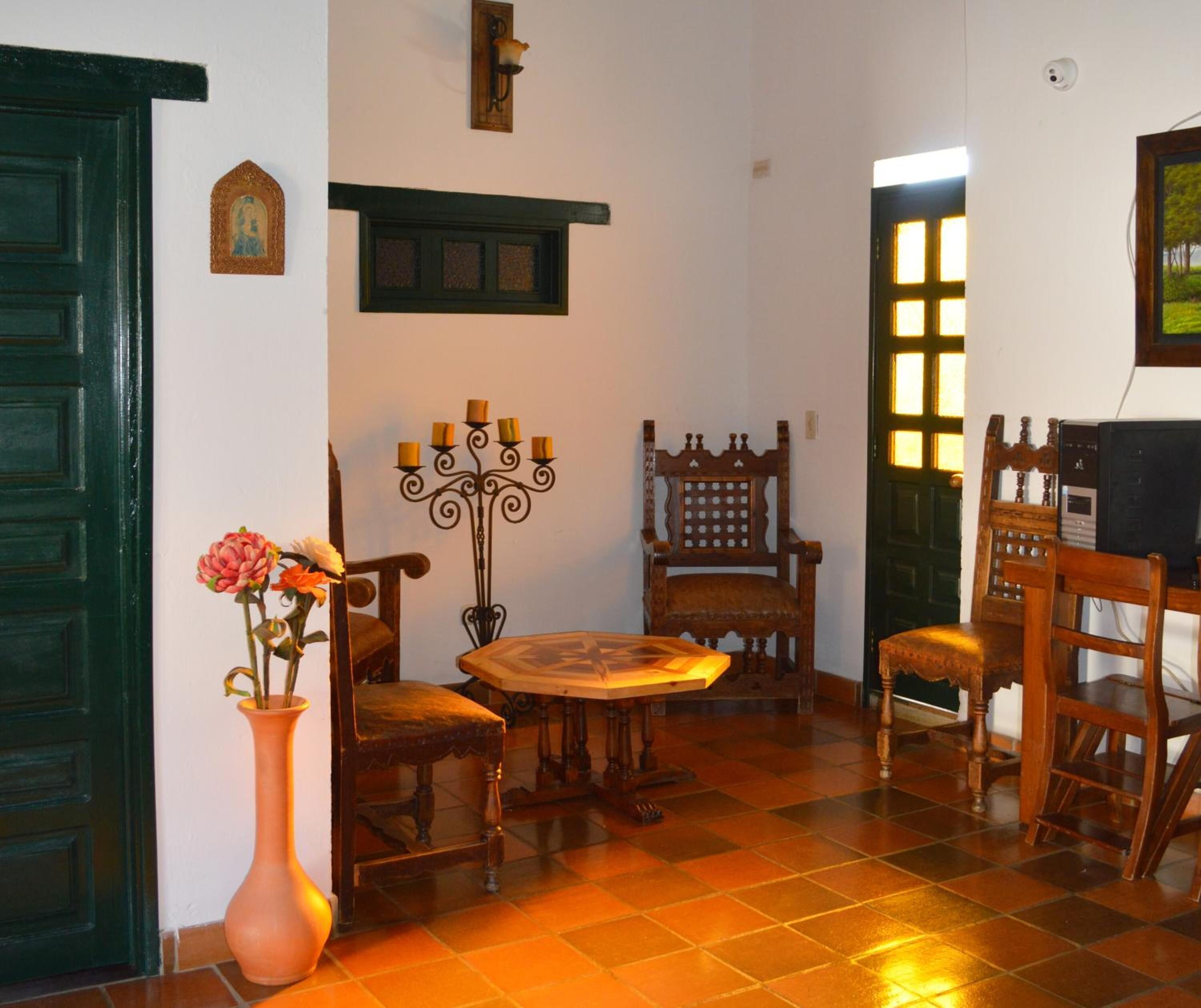 A room with a wooden table, two chairs, a vase with flowers, a wall-mounted candelabra, and a door with a window.