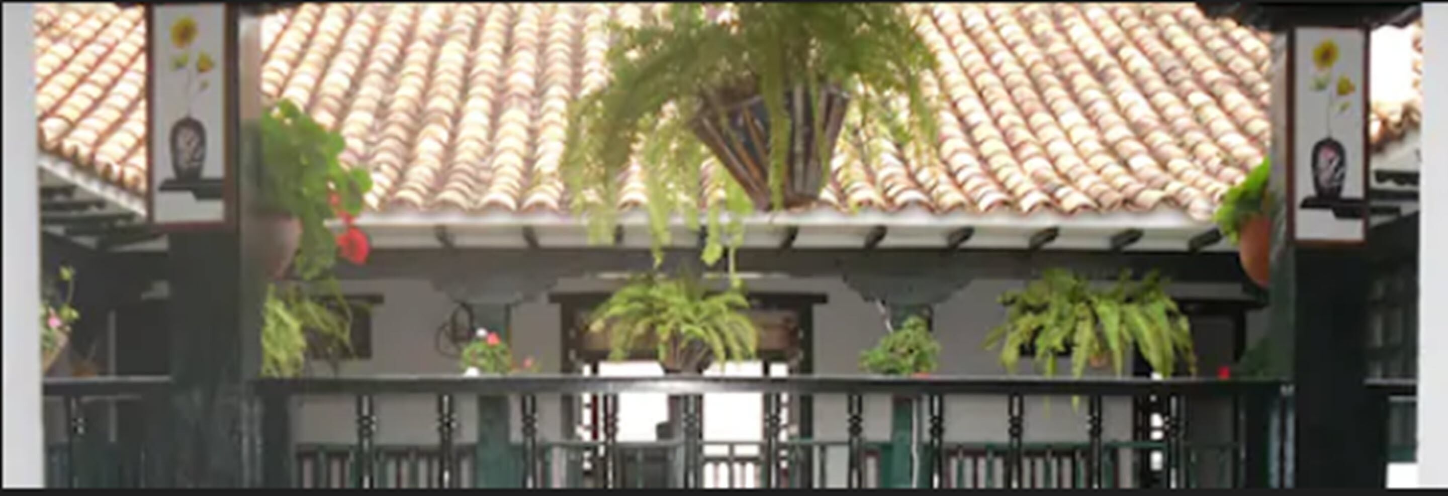 Un bâtiment avec un toit recouvert de tuiles, un balcon orné de plantes et une clôture.