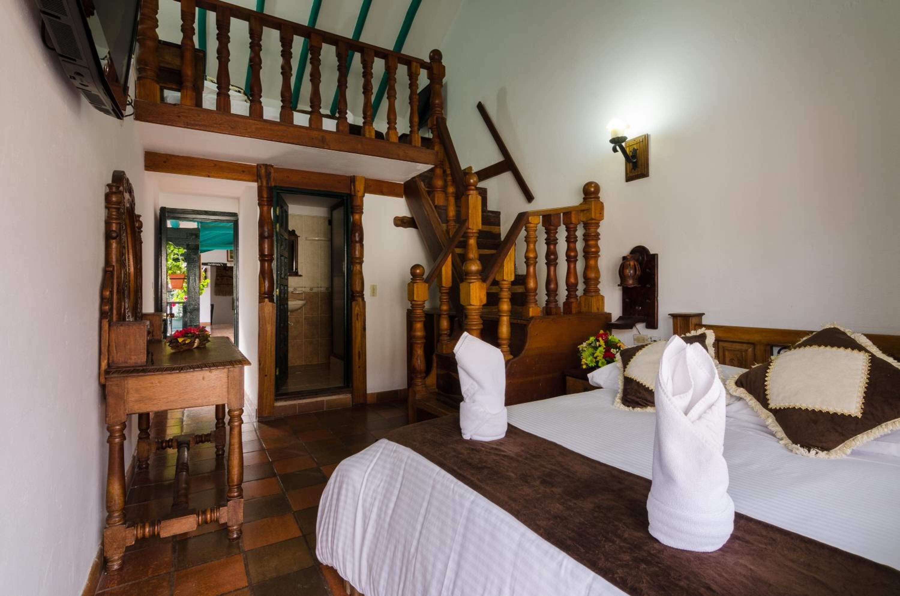 A hotel room with a wooden staircase, a bed with white and brown bedding, and a wooden nightstand with a lamp.