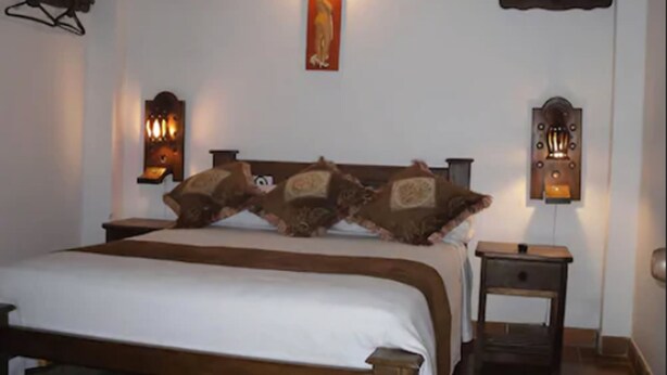 A bed with a wooden headboard, two wall-mounted lamps, and a nightstand with a drawer. - Hotel Antonio Nariño (Villa de Leyva)