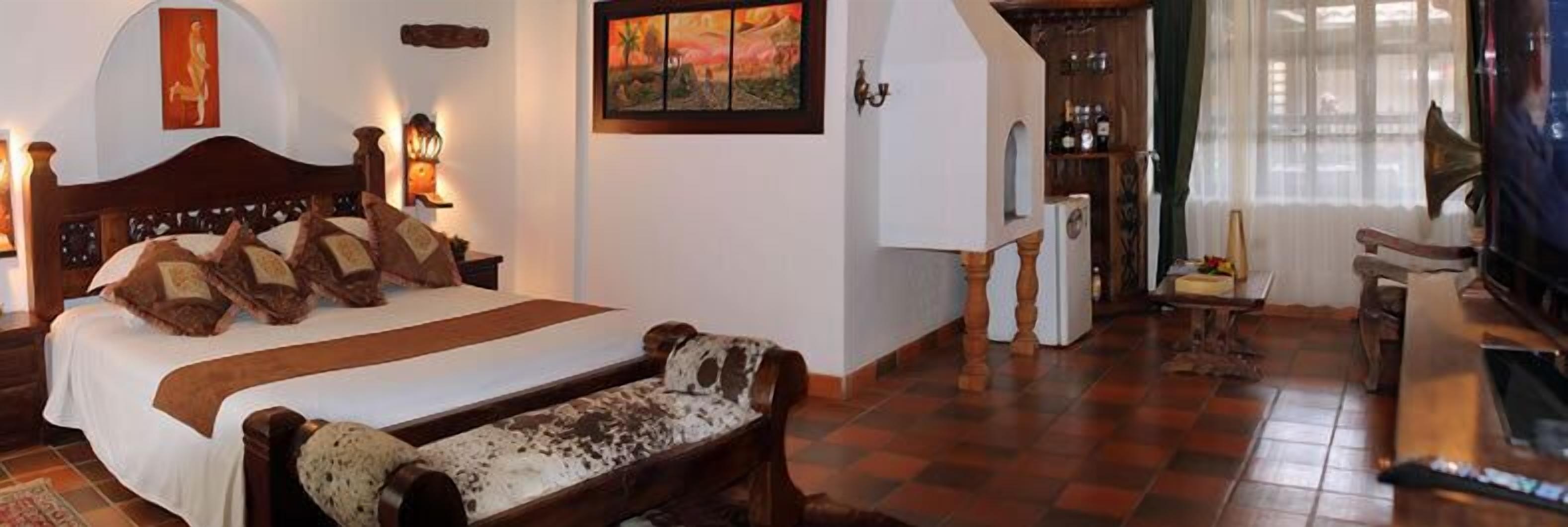 A bedroom with a large bed, a wooden bench, a fireplace, and a wine rack.