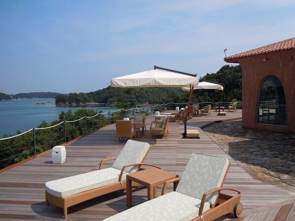 Terraza de madera con sillones de descanso y sombrillas, con vista a una masa de agua.
