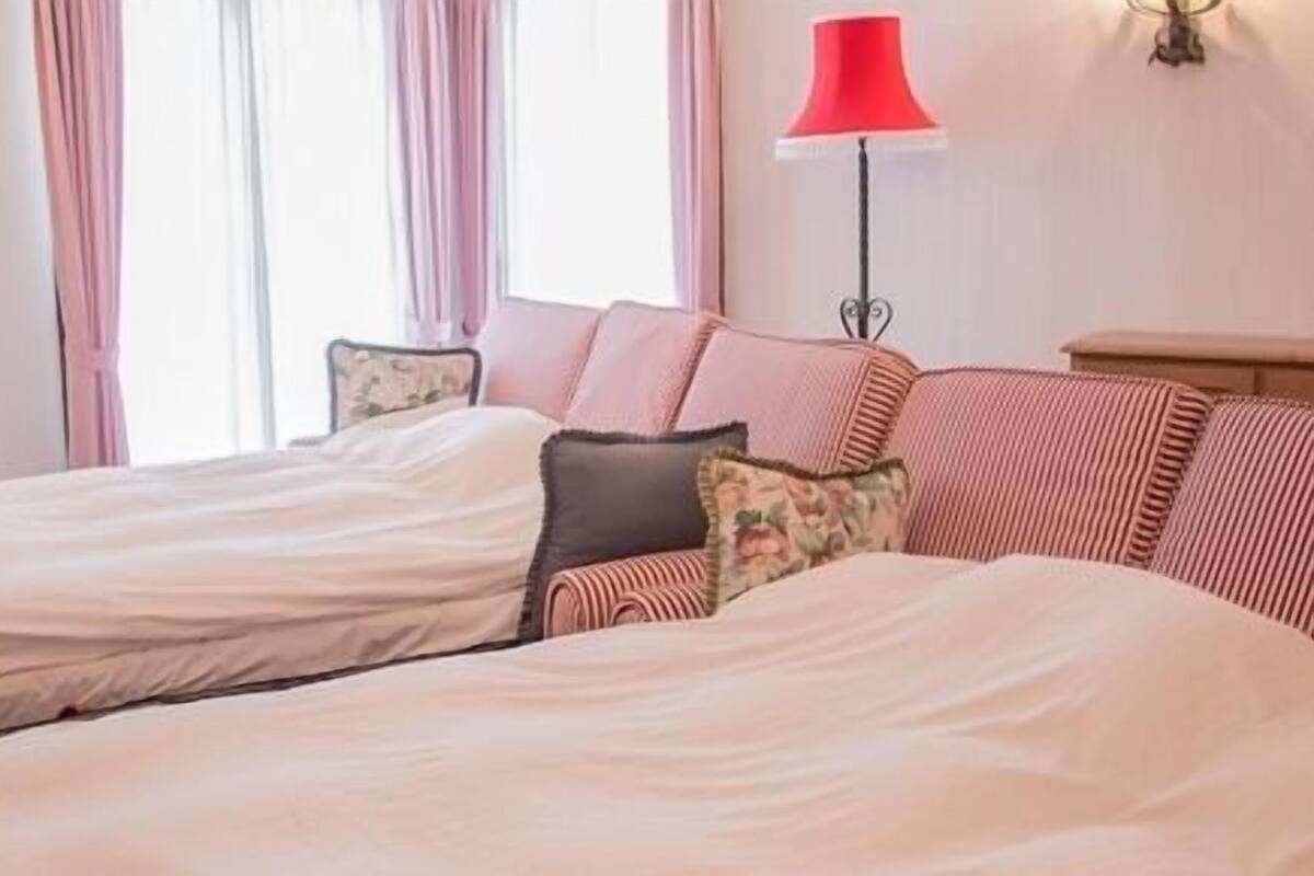 Habitación de hotel con dos camas, una lámpara roja y cortinas rosadas.
