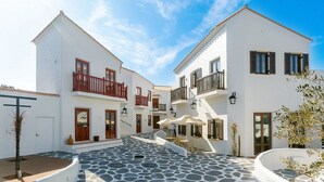 A white building with balconies, a stone courtyard, and outdoor seating. - Shima Mediterranean Village (Shima)