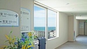 A hotel corridor with directional signs for rooms and a large window offering a view of the sea. - Hotel Miyuki (Wakkanai)
