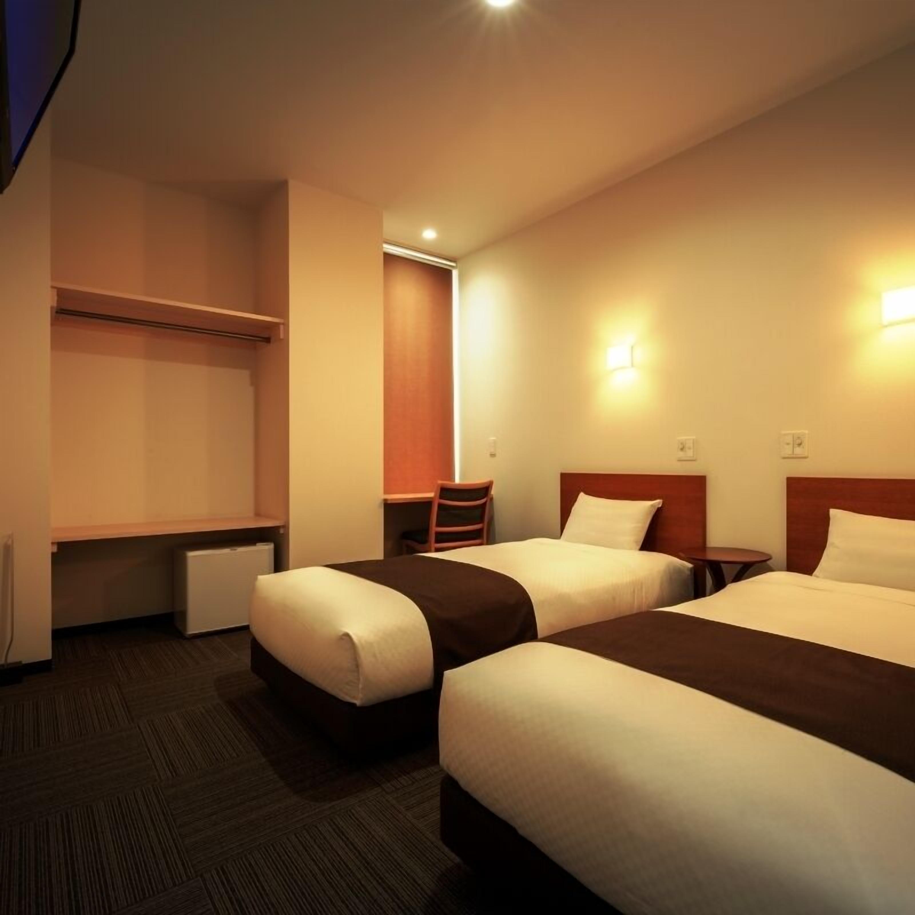 A hotel room with two beds, a desk, and a chair.