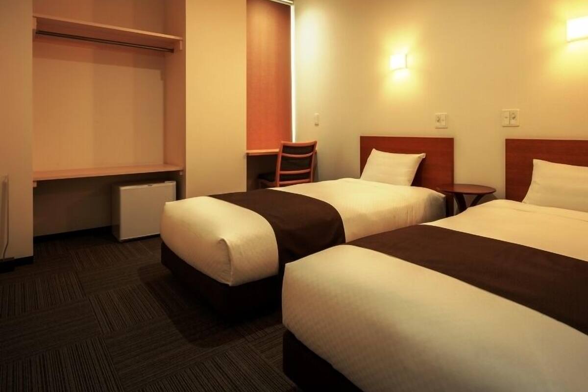 A hotel room with two beds, a desk, and a chair.