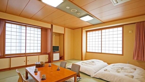 A traditional Japanese room with tatami flooring, a low table with cushions, and a futon bed. - Hotel Miyuki (Wakkanai)