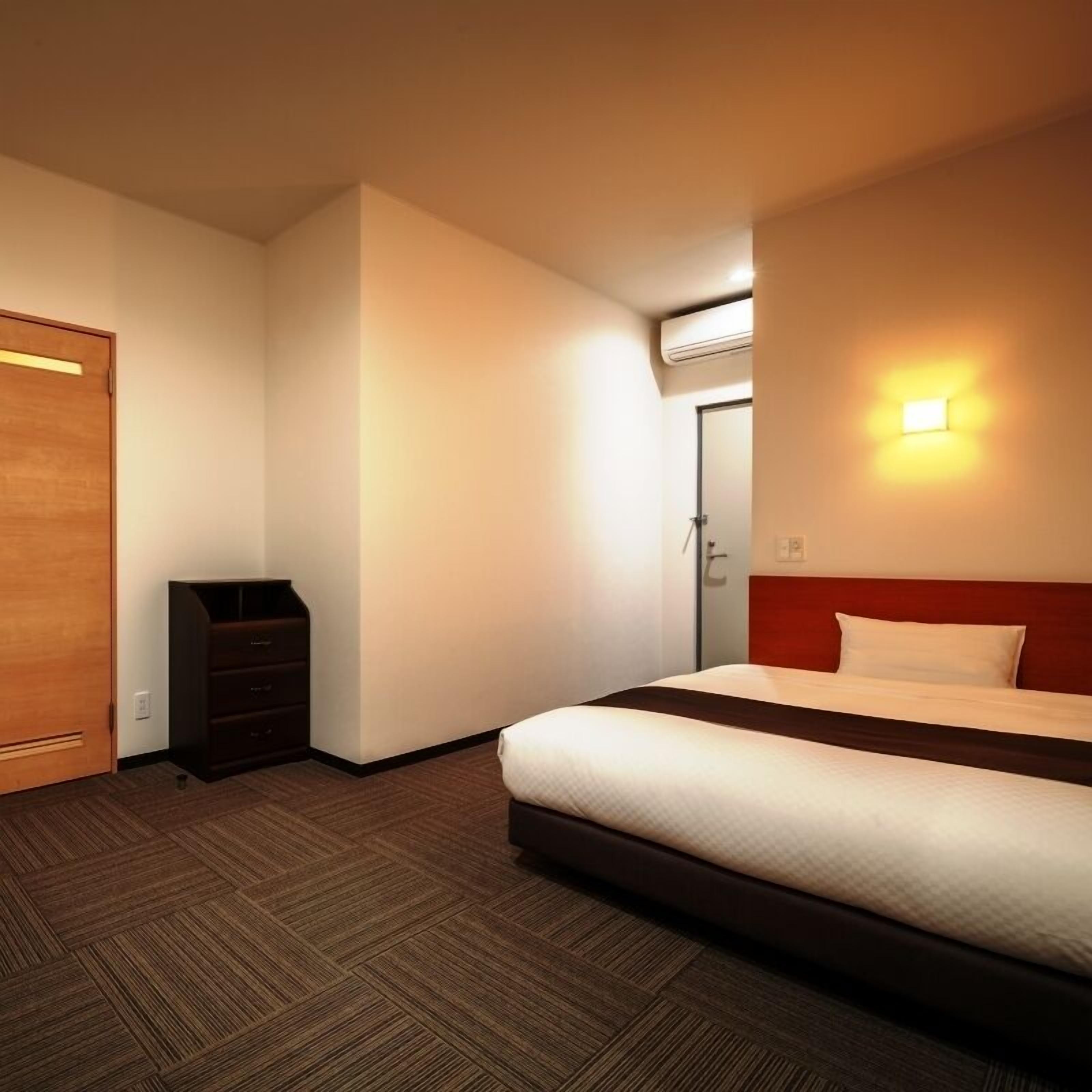 A hotel room with a bed, a dresser, a wardrobe, and an air conditioning unit.
