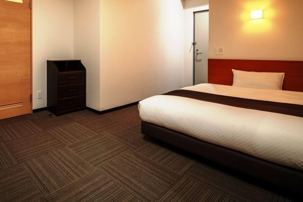 A hotel room with a bed, a dresser, a wardrobe, and an air conditioning unit.