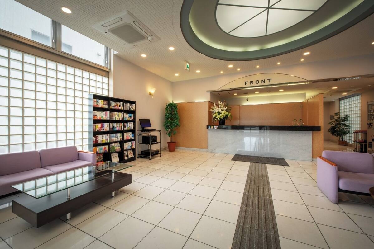 A modern lobby with a reception desk, two sofas, a bookshelf, and a large window.