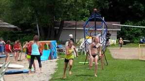 Une plage de sable où se trouvent des enfants et des adultes, dont certains portent des gilets de sauvetage, et où l’on aperçoit, au fond, une structure de jeux pour enfants.