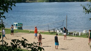 Un match de volleyball de plage se déroule sur un terrain de sable, avec un lac en arrière-plan.