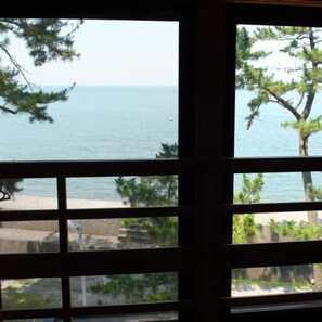 A view through a window with a grid pattern, overlooking a beach and the sea. - Nisshokan (Ise)