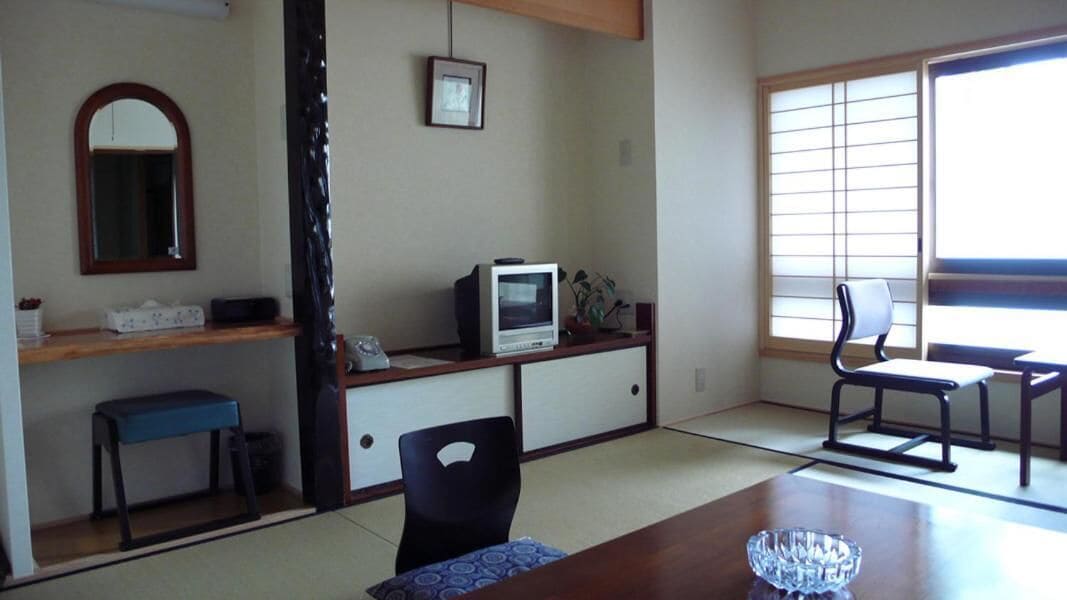 Een traditionele Japanse kamer met tatami vloerbedekking, een lage tafel met een glazen schaal, een televisie op een kast, een blauwe bank en een schuifdeur.