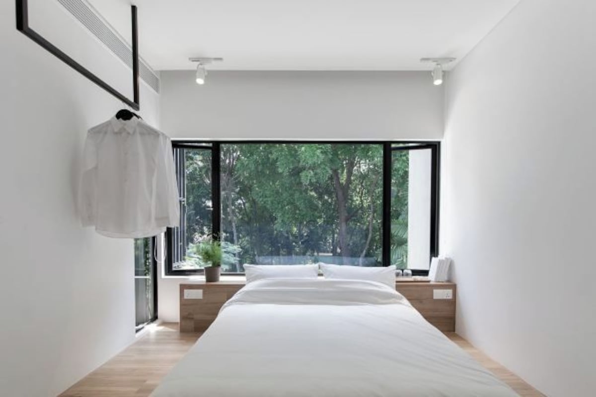Un dormitorio moderno con una cama grande, vistas a la vegetación a través de amplias ventanas y un diseño minimalista.