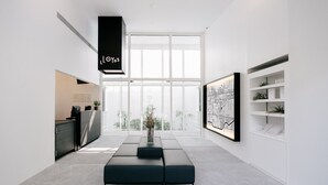 Habitació moderna i minimalista amb una finestra gran, una làmpada penjant negra, un sofà fosc i una estant mural decorativa.