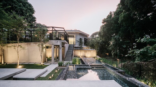 Edifici modern amb una escala que condueix a un segon pis, envoltat de vegetació i una zona de piscina.