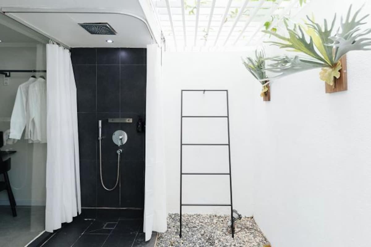 Un baño moderno con zona de ducha, un perchero blanco y plantas decorativas.
