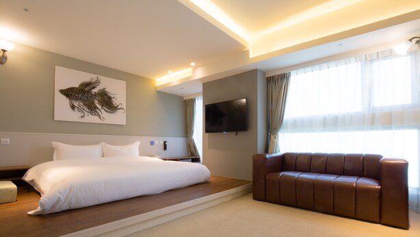 A hotel room with a bed, a brown leather sofa, a flat-screen TV, and a wall-mounted artwork. - Walker Hotel Ximen (Taipei)