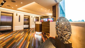 A modern hotel lobby with a colorful striped floor, elevators, a reception desk, and a large abstract sculpture. - Walker Hotel Ximen (Taipei)