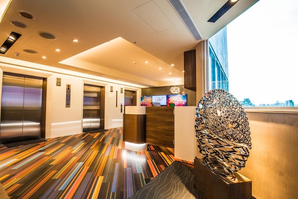 A modern hotel lobby with a colorful striped floor, elevators, a reception desk, and a large abstract sculpture. - Walker Hotel Ximen (Taipei)