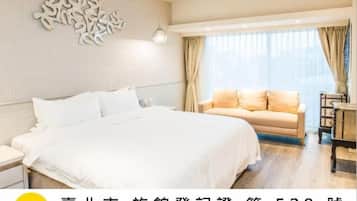 Habitación de hotel con una cama grande, un sofá, un adorno de pared y una ventana con cortinas.