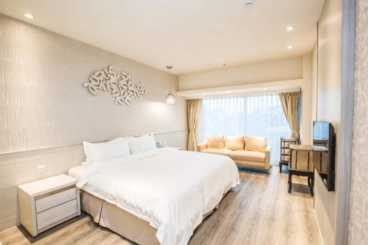 A modern hotel room with a large bed, a sofa, a desk, and a decorative wall piece.