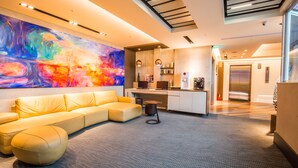 A modern living area with a sofa, ottoman, and a colorful abstract painting on the wall. - Walker Hotel Ximen (Taipei)