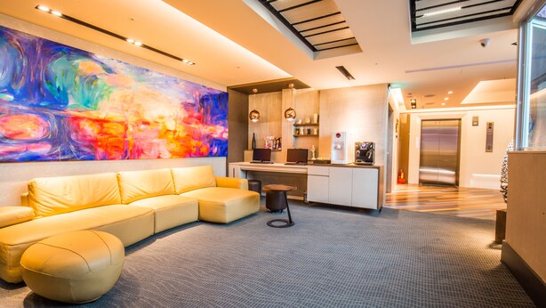 A modern living area with a sofa, ottoman, and a colorful abstract painting on the wall. - Walker Hotel Ximen (Taipei)