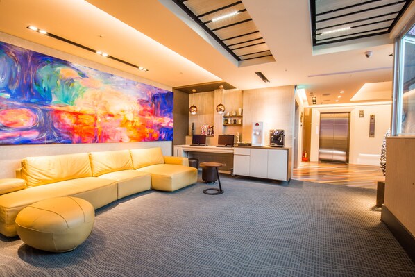 A modern living area with a sofa, ottoman, and a colorful abstract painting on the wall. - Walker Hotel Ximen (Taipei)