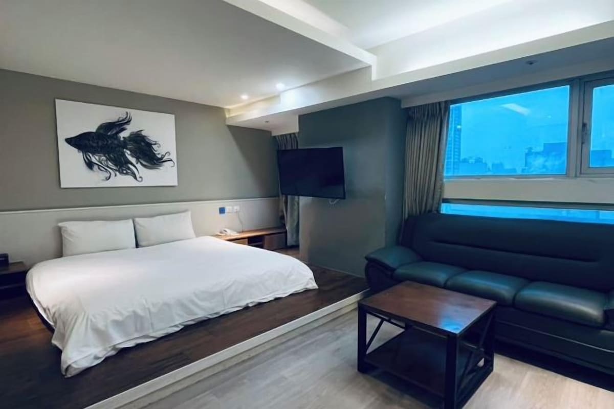A hotel room with a bed, a sofa, a coffee table, a flat-screen TV, and a city view.