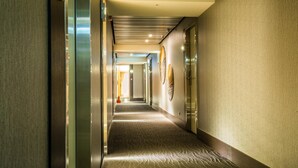 A hotel corridor with a patterned carpet, metallic elevator doors, and wall-mounted artwork. - Walker Hotel Ximen (Taipei)