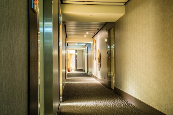 A hotel corridor with a patterned carpet, metallic elevator doors, and wall-mounted artwork. - Walker Hotel Ximen (Taipei)