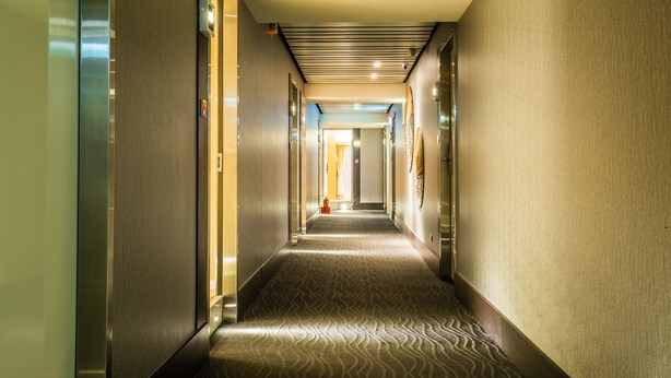 Un pasillo de hotel con alfombra estampada, puertas a ambos lados y un techo con iluminación empotrada.