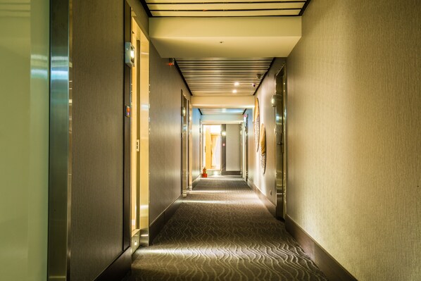 A hotel hallway with a patterned carpet, doors on both sides, and a ceiling with recessed lighting. - Walker Hotel Ximen (Taipei)