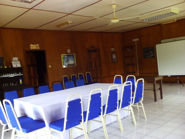 Un salón de conferencias con una larga mesa y sillas azules, paredes de madera y una pizarra.