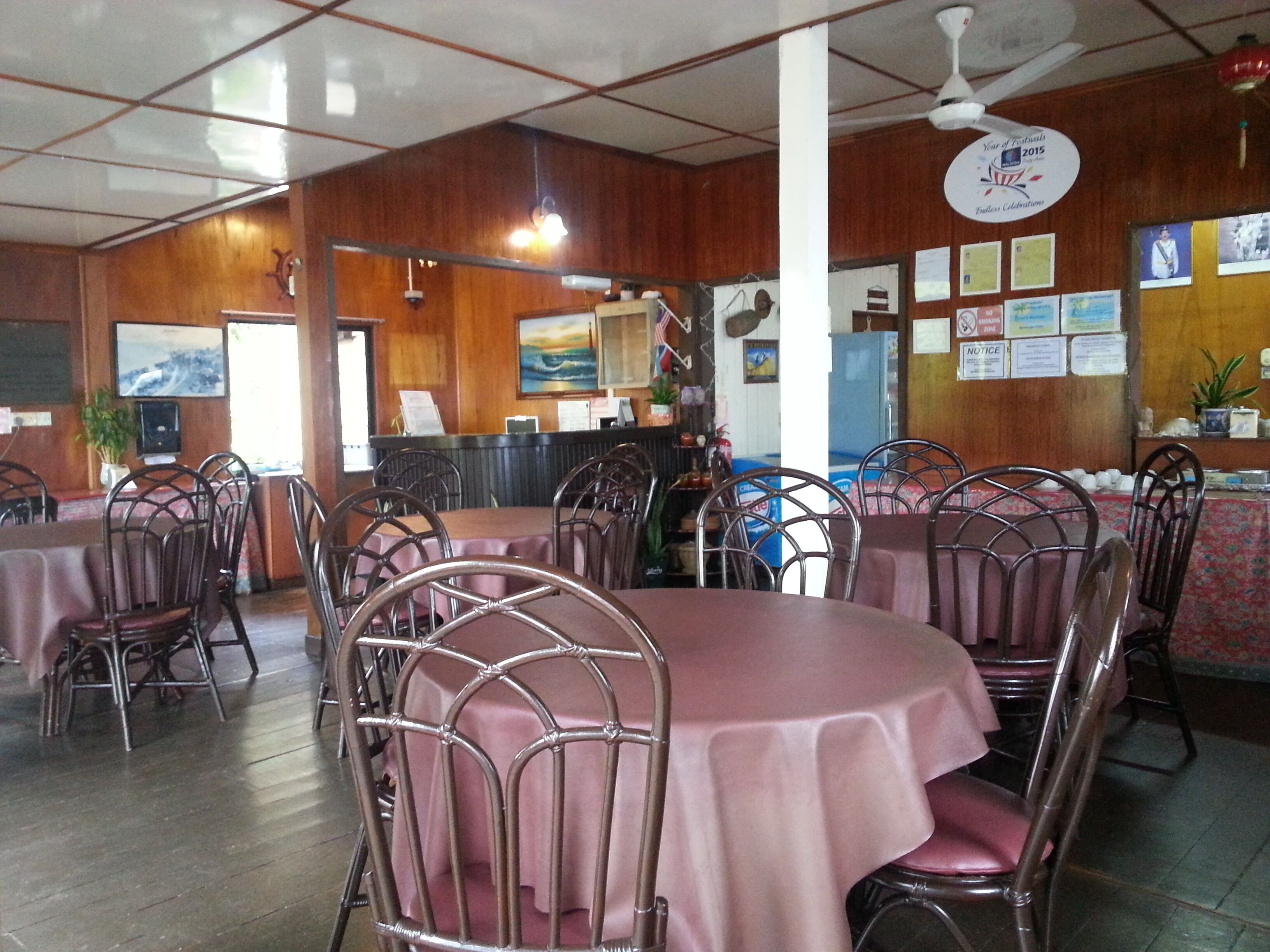 A restaurant with round tables covered in pink tablecloths and metal chairs. There are wooden walls and a ceiling fan.