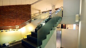 A modern interior with a glass staircase, a brick wall, and a well-lit area with a counter. - Hotel Nyland Cipaganti (Bandung)